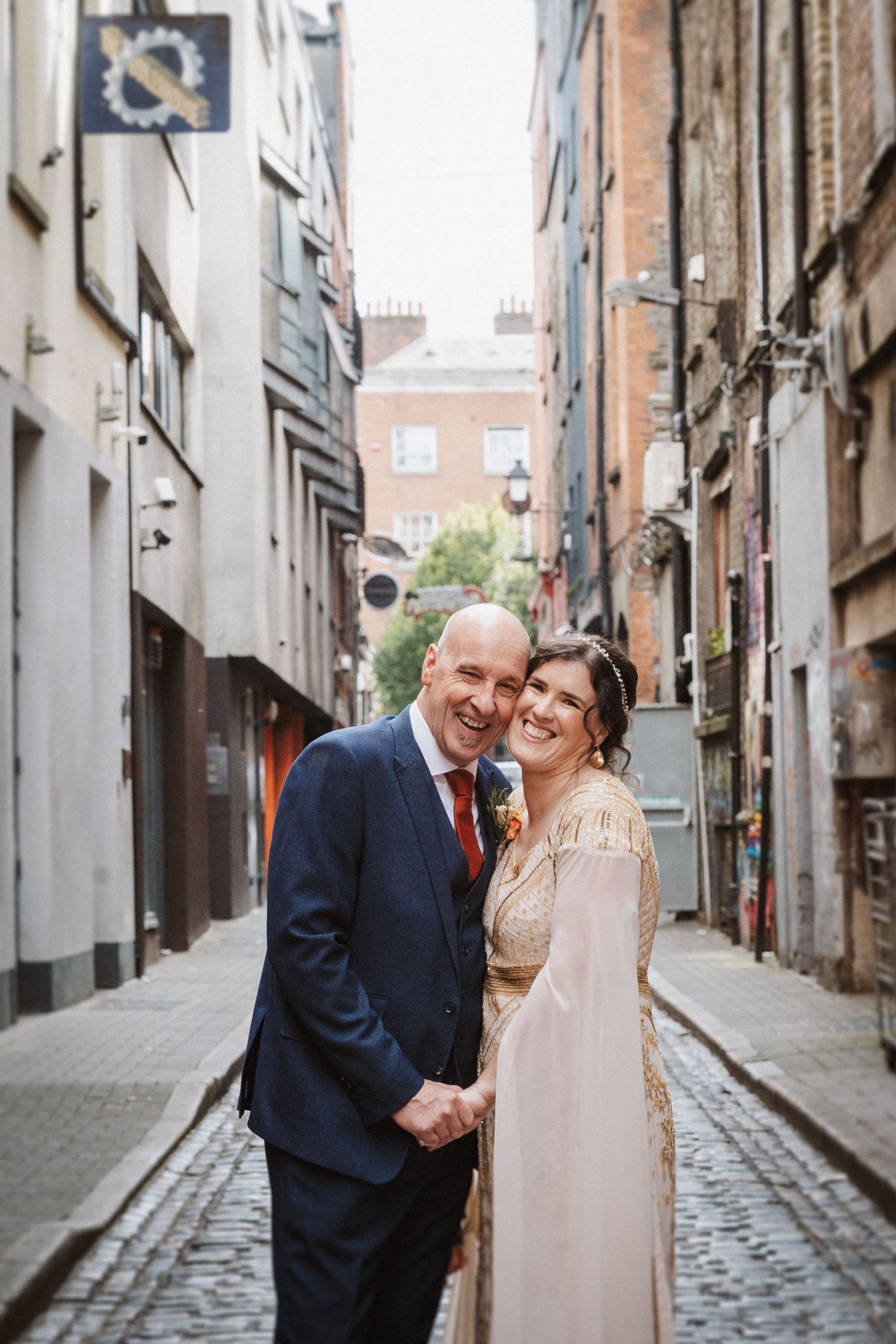 A couple shares an intimate moment on a charming cobblestone alley between historic buildings.