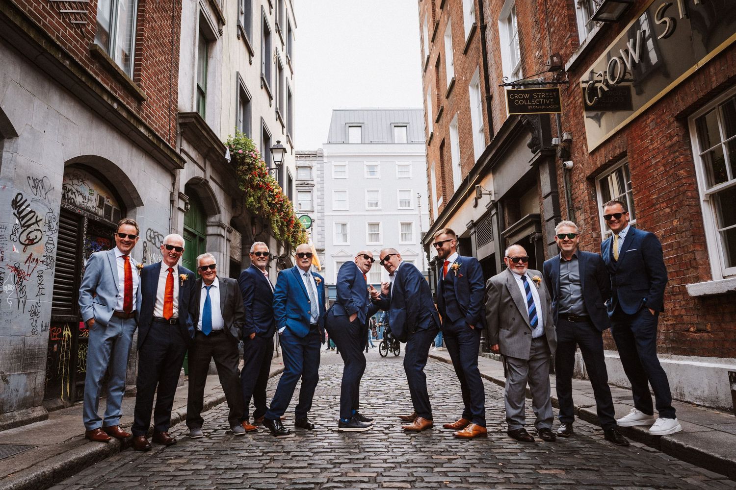 Wedding guests gather in a narrow cobblestone alley between brick buildings during an urban celebration.