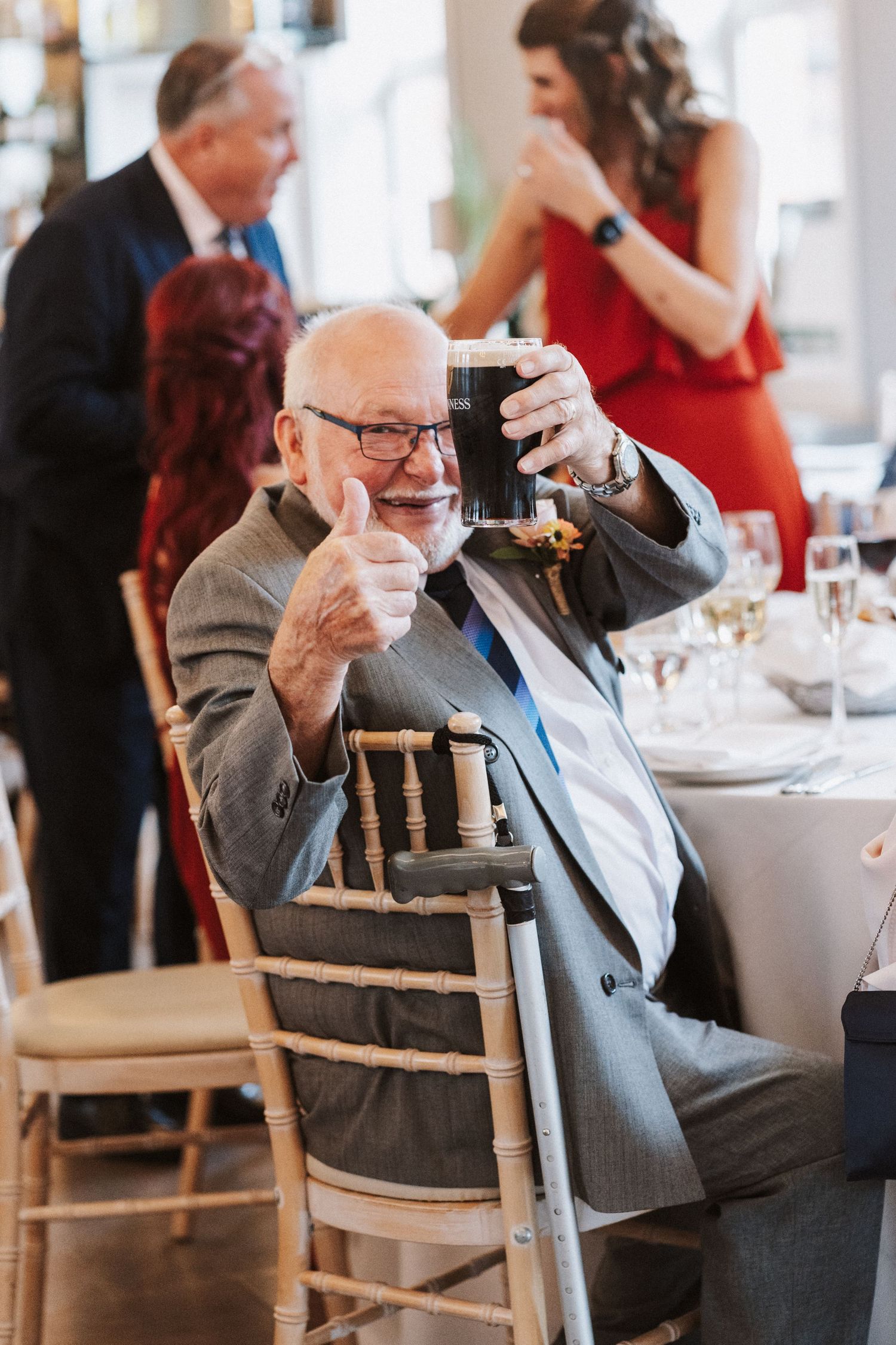 Elderly gentleman in a suit raises his glass with a cheerful expression at an elegant dining event.