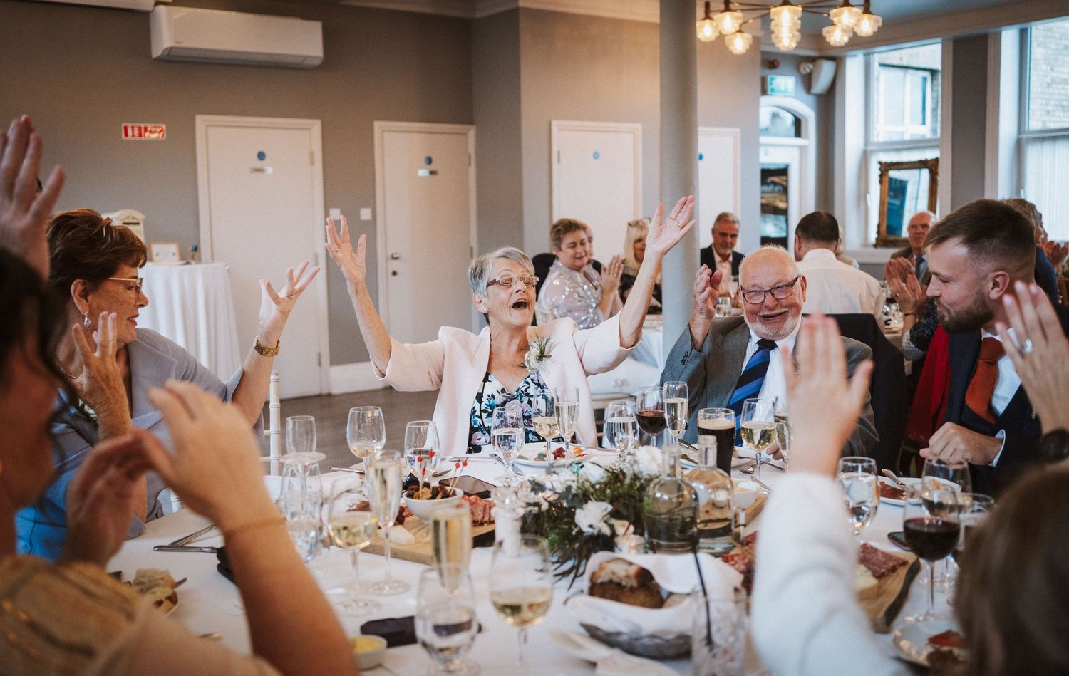 Wedding guests raise their glasses in celebration during a toast at an elegant indoor reception.