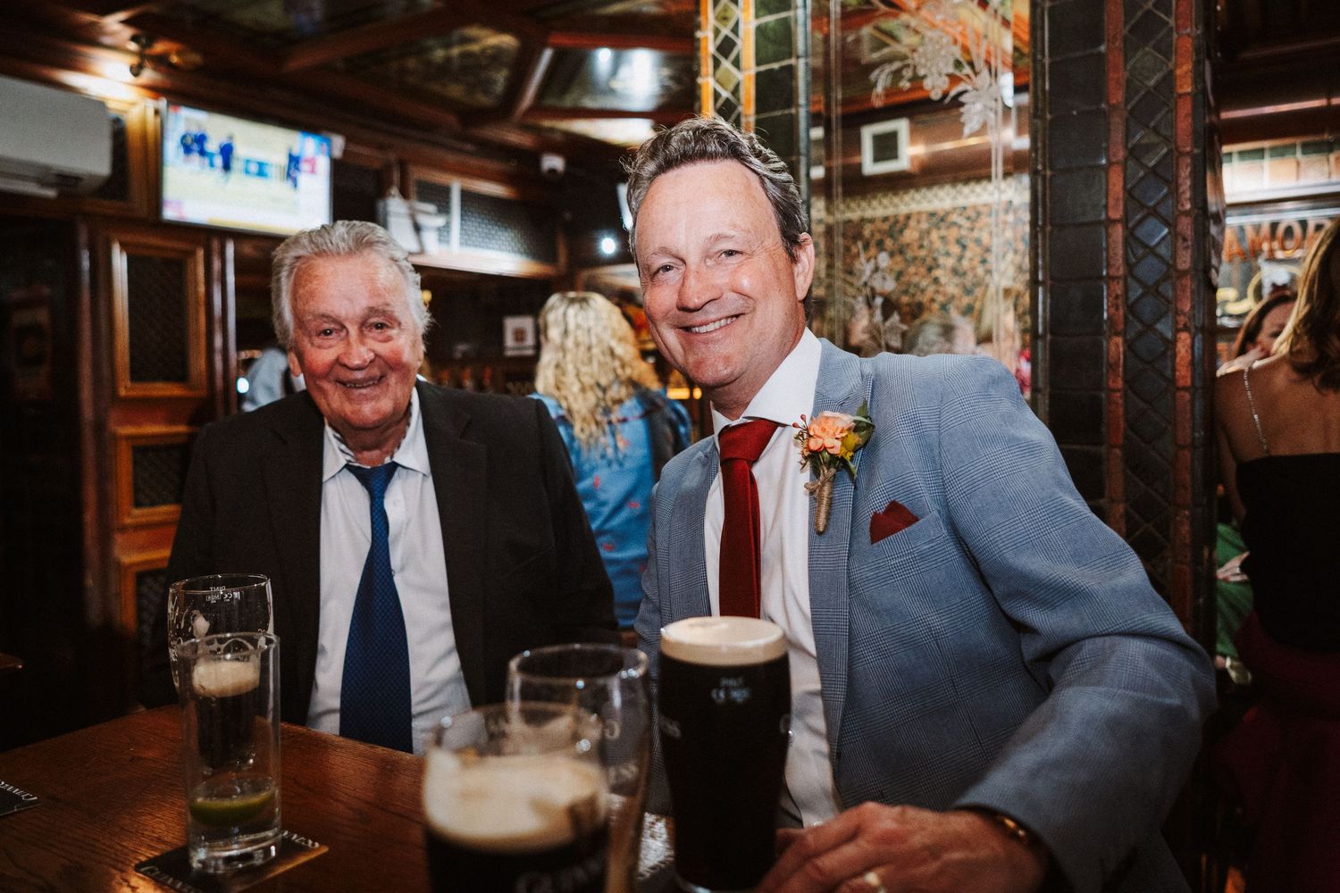 Friends enjoying drinks and conversations at a traditional pub, raising beer glasses in celebration at a dimly lit bar.
