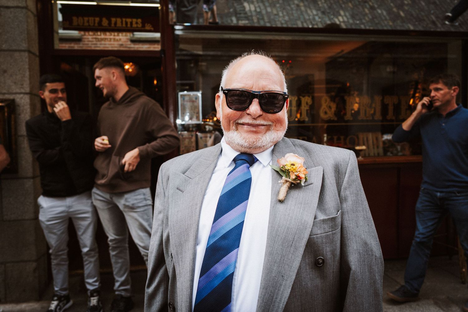 Wedding guest in a grey suit and blue striped tie poses at an indoor venue.