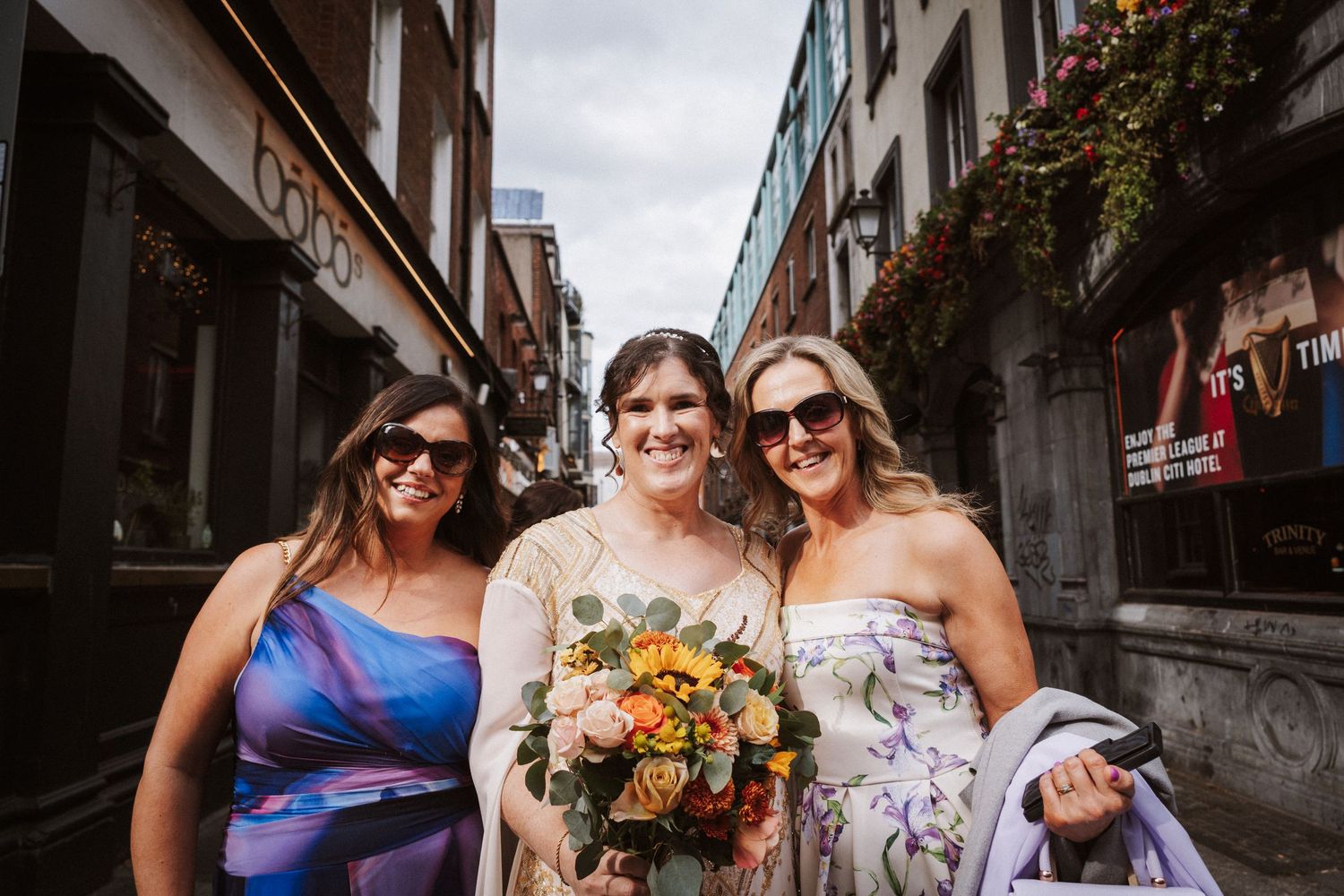 Friends in colorful dresses celebrate at a rustic outdoor venue decorated with flowers and autumn decor.