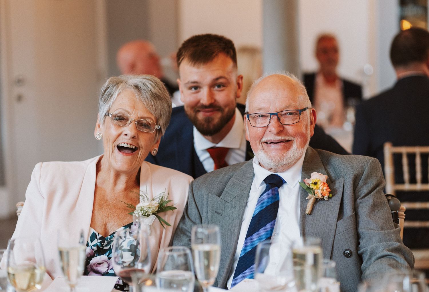 Wedding guests seated at reception tables share laughter and conversation during an elegant indoor celebration.