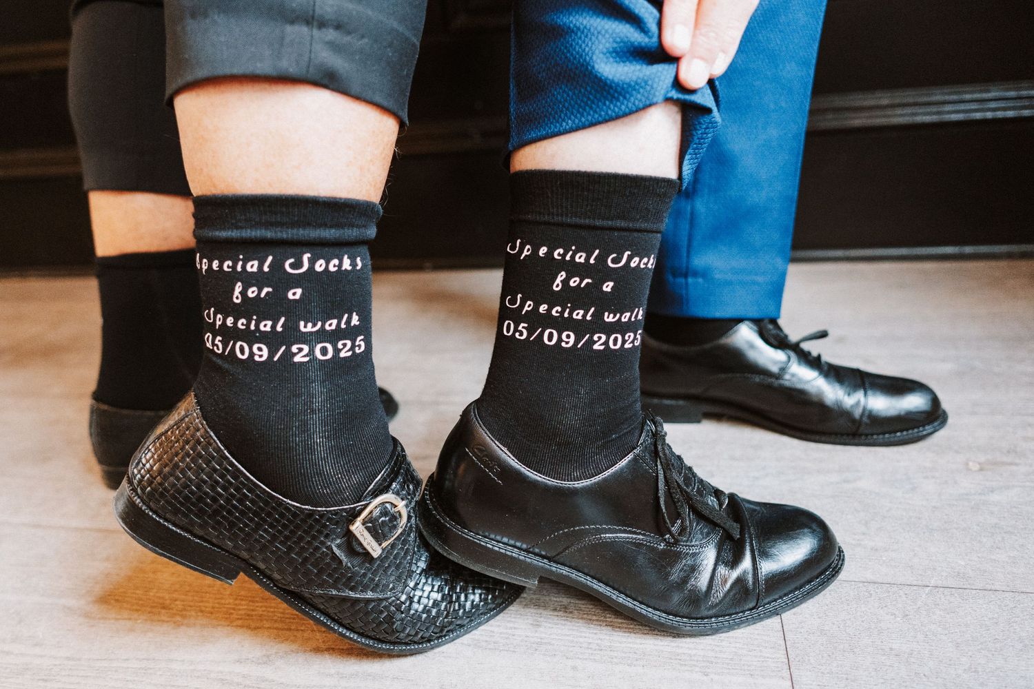 Black leather cowboy boots with white socks displaying text decoration seen from different angles on wooden floor.