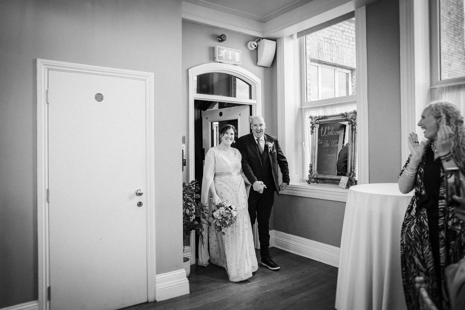 Black and white photograph showing the interior hallway of a house with doorways and natural light streaming in through windows.