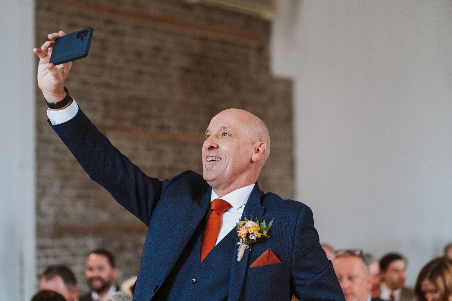 Wedding guests cheer and celebrate while raising their drinks during a joyful reception toast at a rustic brick venue.