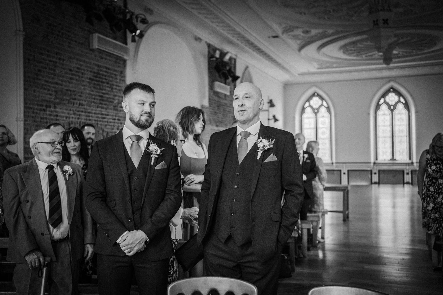 Groomsmen sharing laughter and candid moments during a wedding ceremony in a historic church interior.