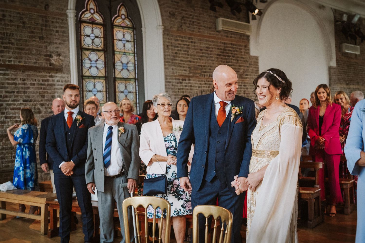 Wedding ceremony taking place inside a historic brick church with stained glass windows and wooden pews.