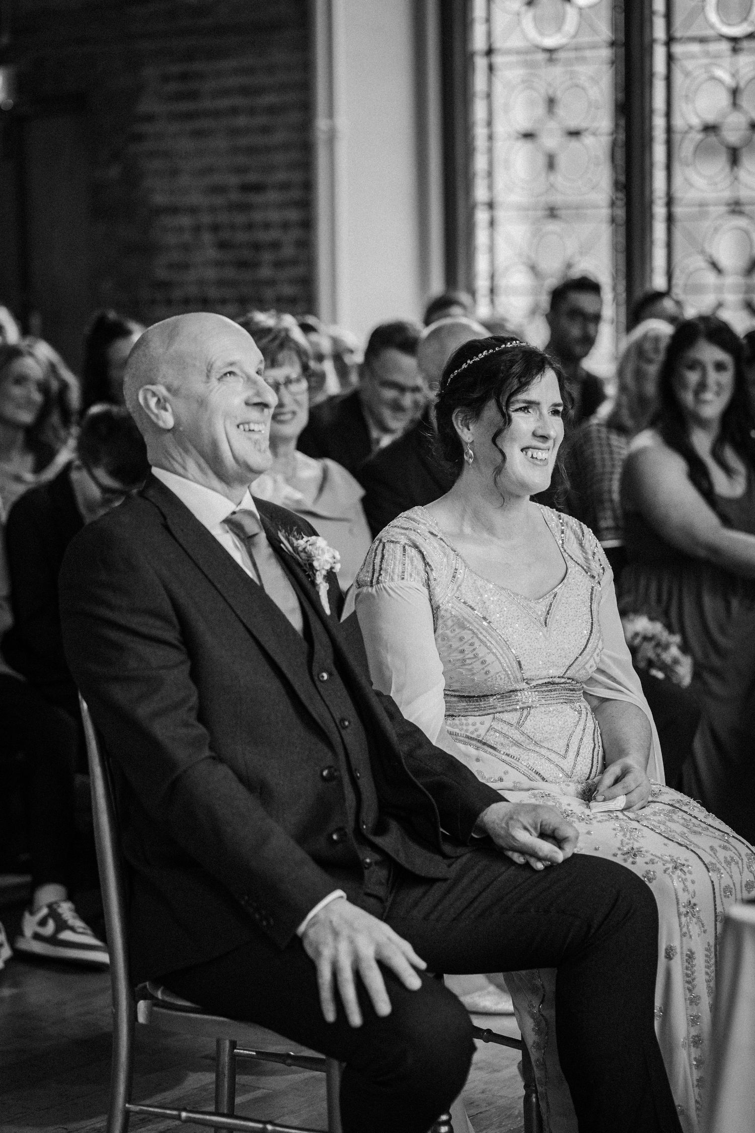 A laughing couple sits together at a formal event, showing joyful expressions in a black and white photo sequence.