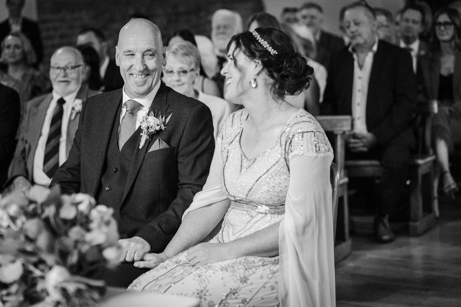 Black and white photograph showing a tender moment during an indoor wedding ceremony.