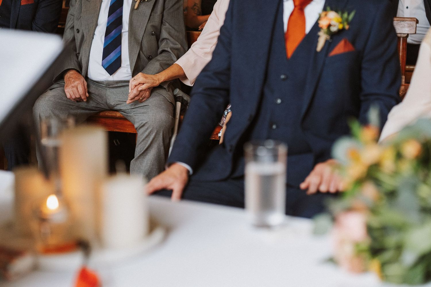 Wedding party groomsmen in gray suits with orange accents stand together during outdoor ceremony.