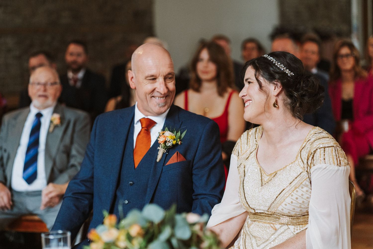 Wedding guests smile and share emotional reactions during a traditional ceremony in an elegant indoor venue.
