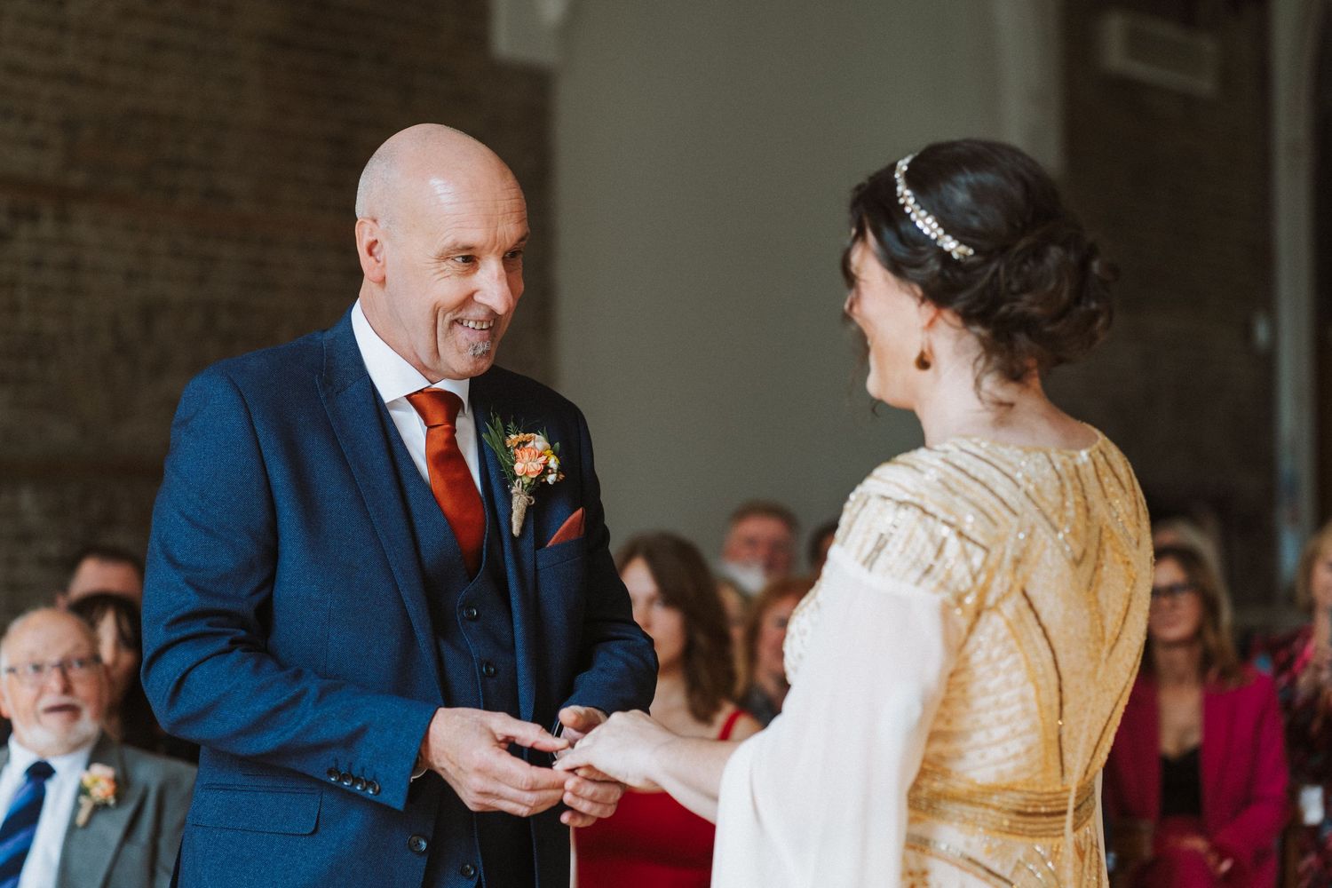 A bride and groom share a candid moment during their wedding celebration as guests look on in the background.