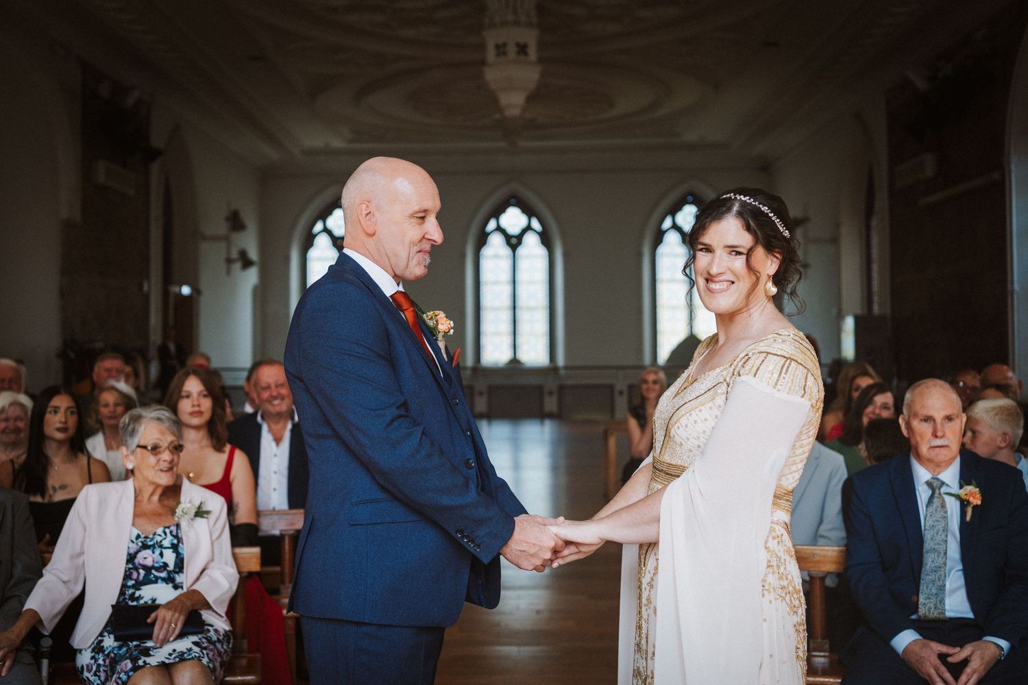 Wedding guests gather in a historic venue with gothic windows to celebrate the newlyweds.