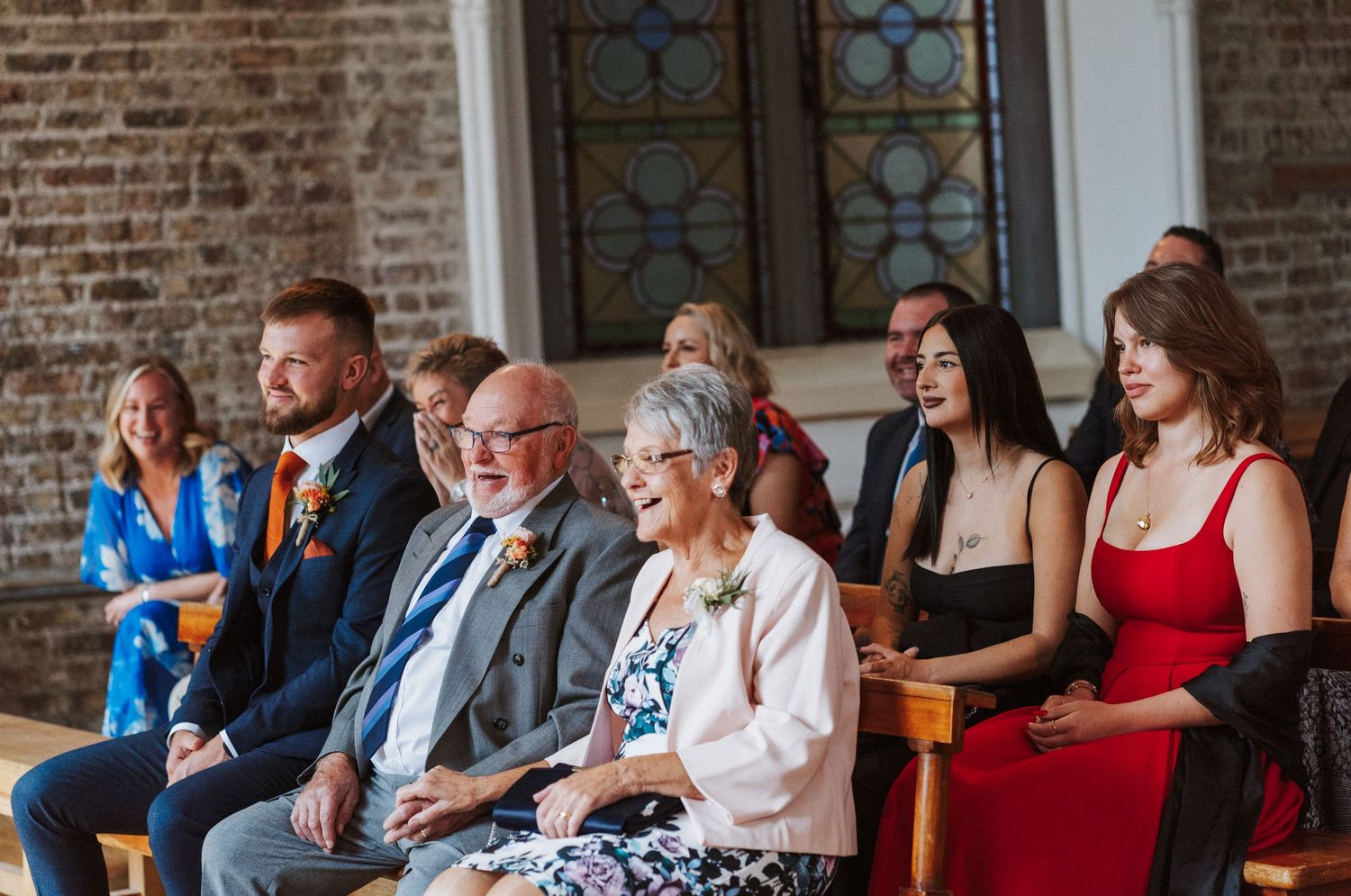 Wedding guests smile and laugh during an emotional ceremony in a historic brick church venue.