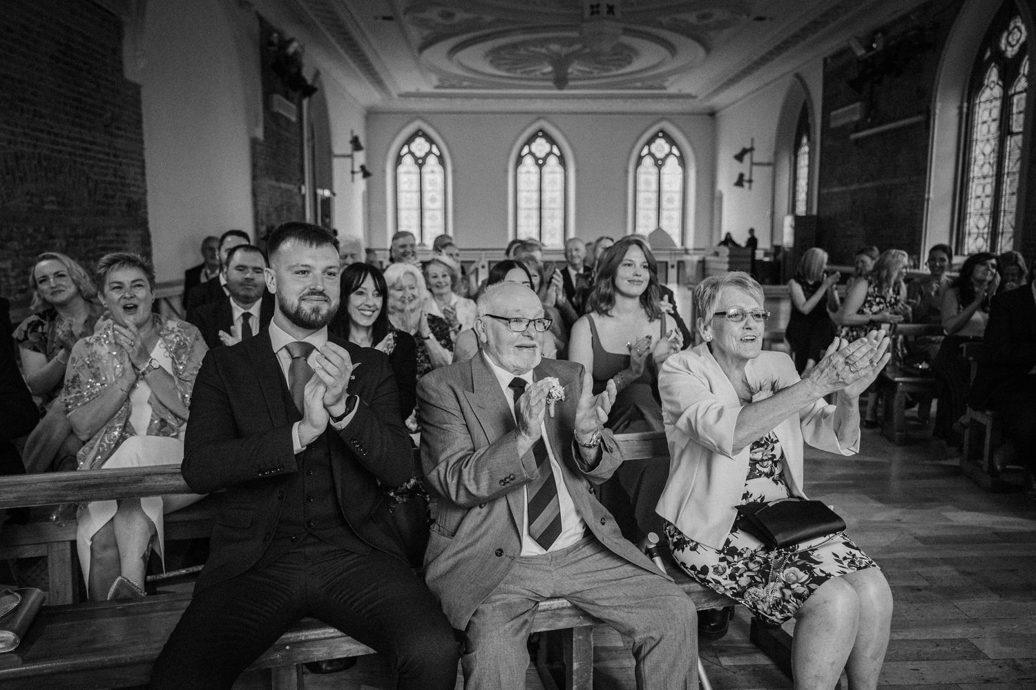 Wedding guests react with laughter and joy during an emotional moment at a church ceremony.