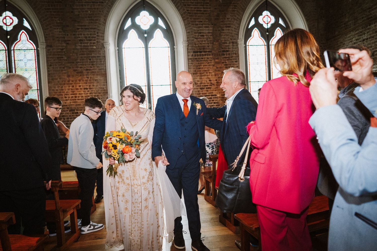 Guests mingle and socialize during an event in a historic church venue with gothic architecture and exposed brick walls.
