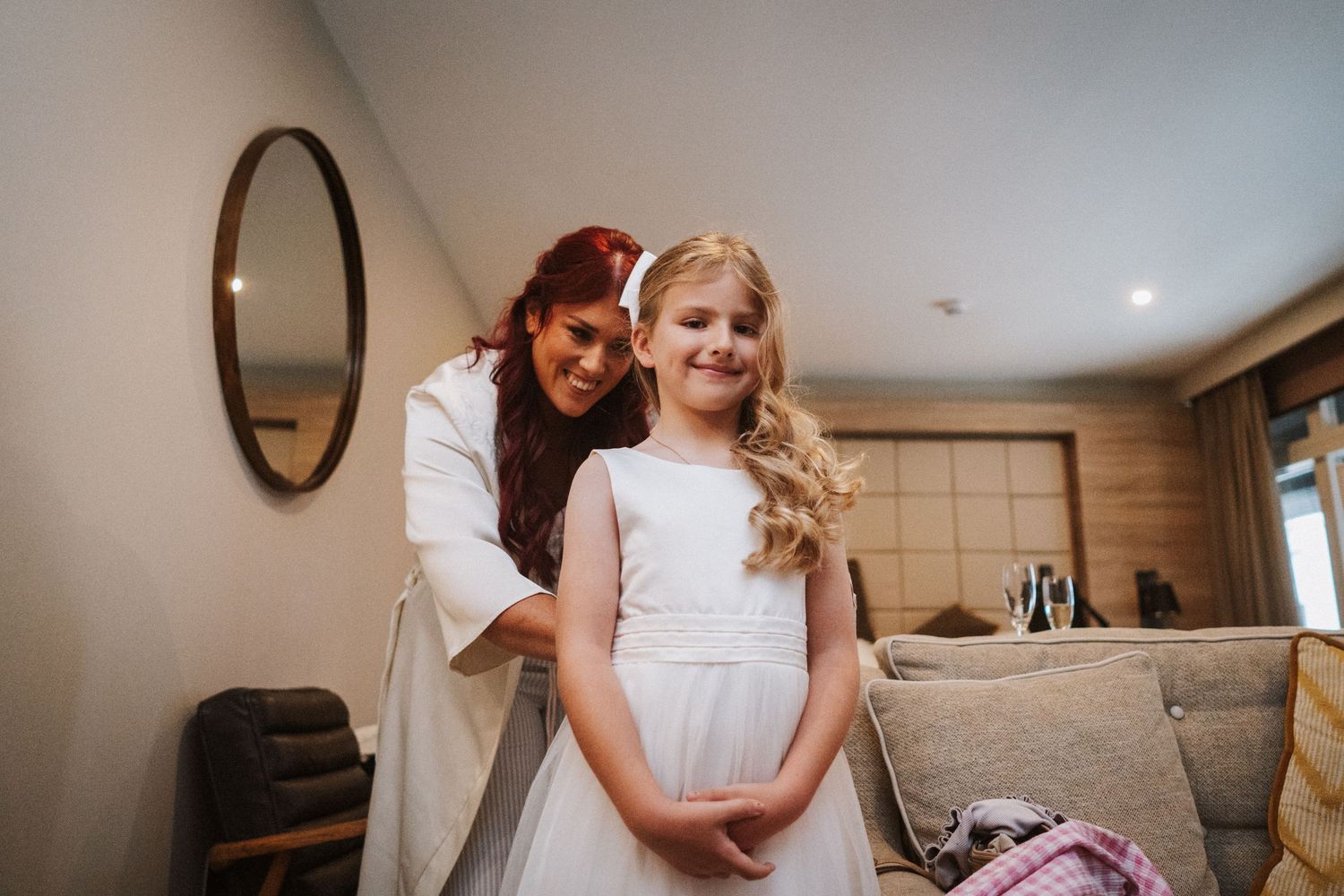 A young flower girl in a white dress sits and plays while getting ready for a formal event.