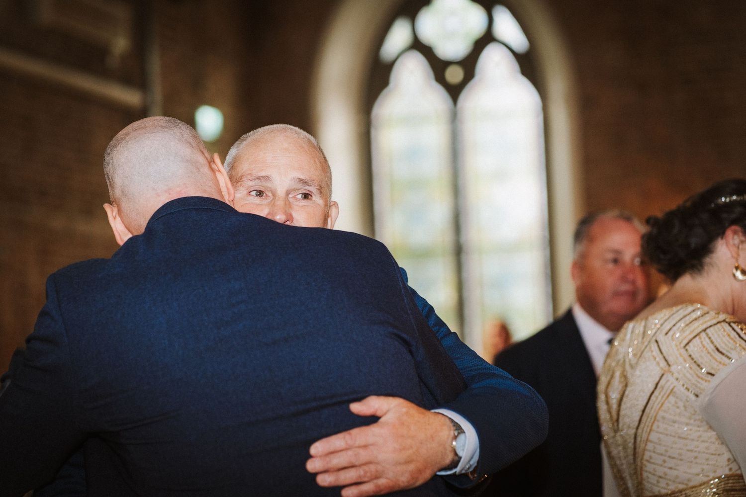 Friends greet each other with warm embraces at a wedding reception in an elegant indoor venue.
