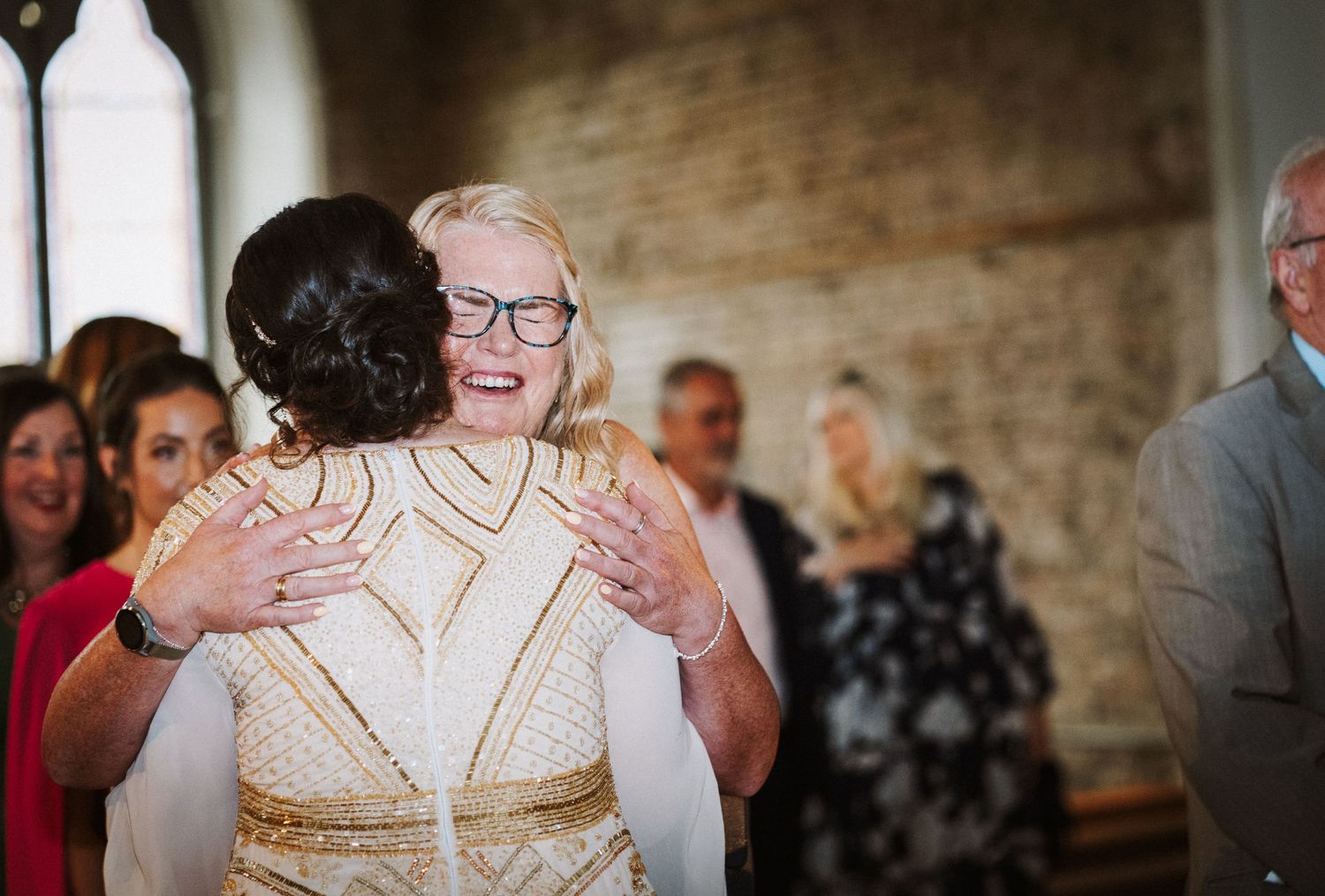 Wedding guests celebrate and dance together during an indoor reception at a rustic brick venue.