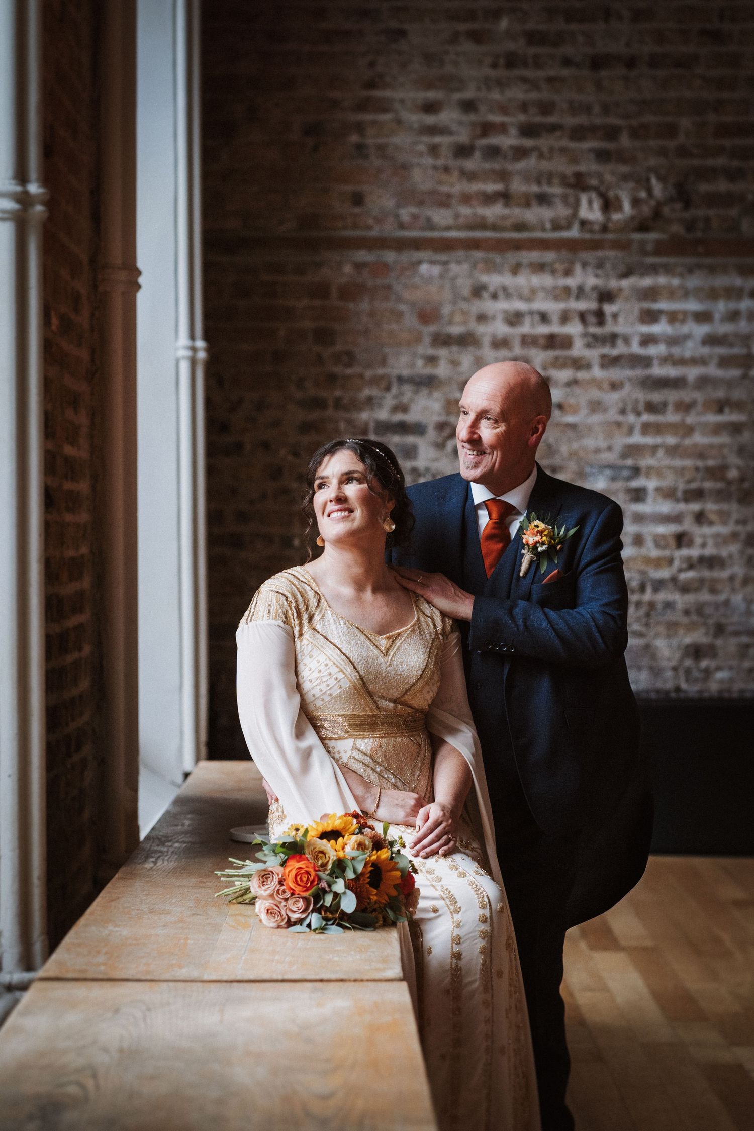 A couple share intimate moments across a dining table in a rustic brick-walled venue.