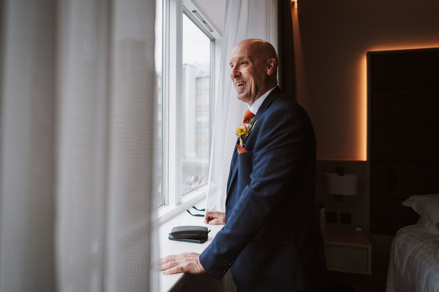 A person in a suit stands by a window looking at papers in an office setting.