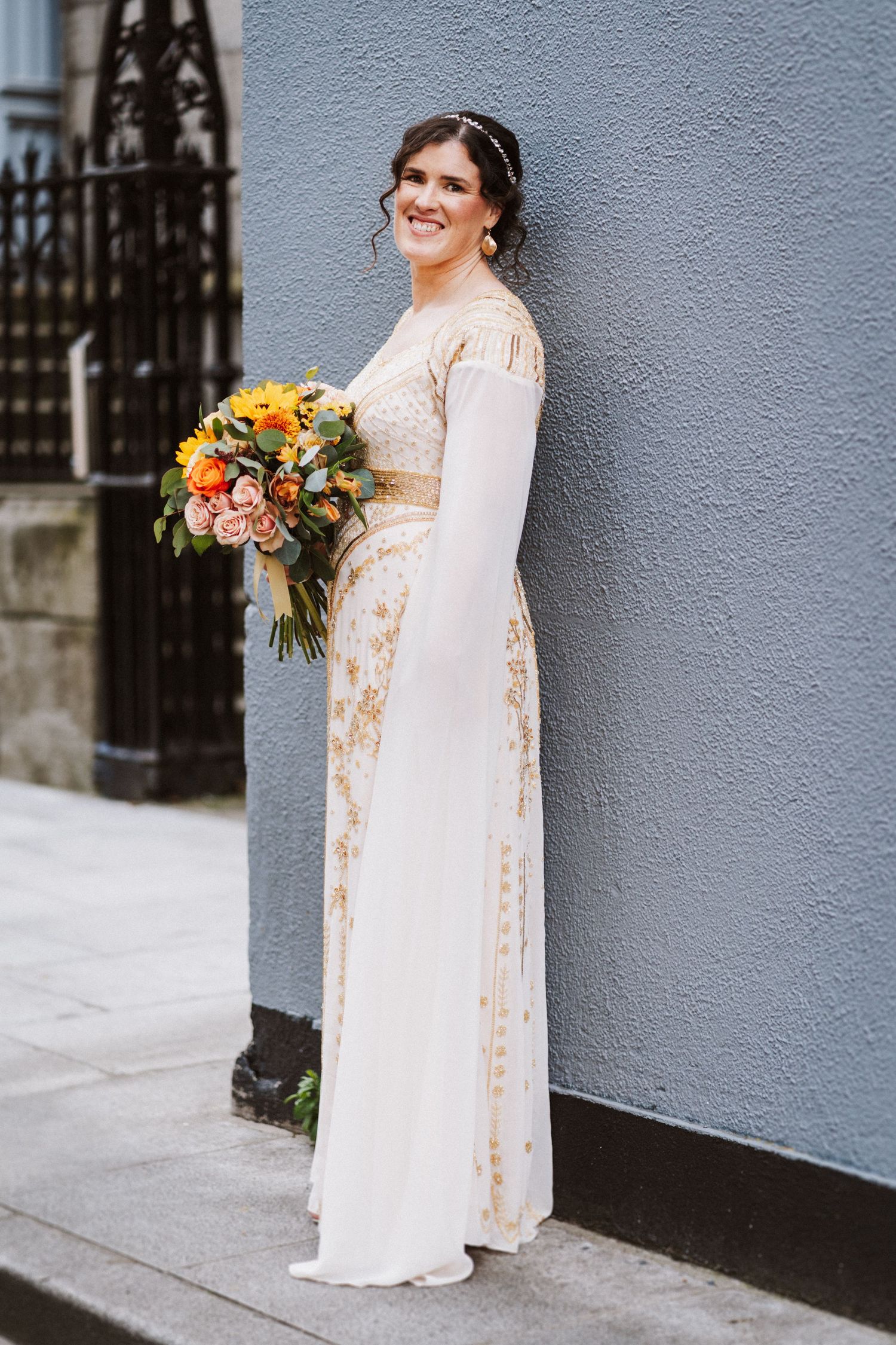 Wedding photos showing a person in a long white floral dress with sheer sleeves holding a bright orange and pink bouquet.