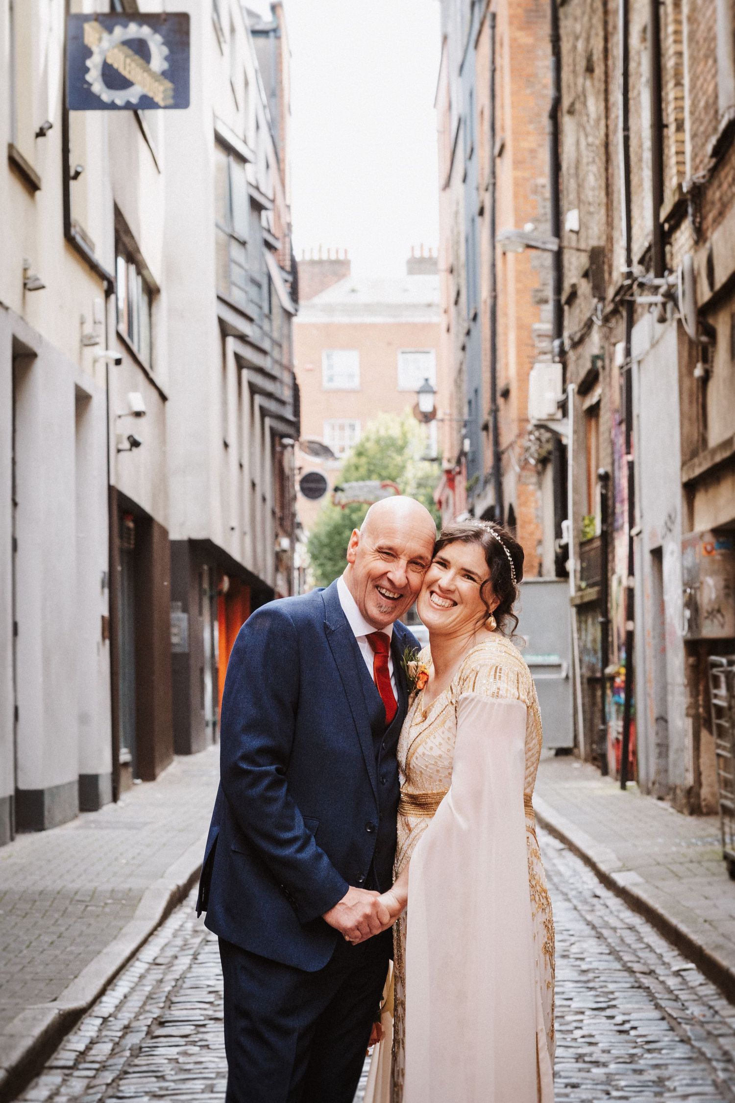 A happy couple shares loving moments on a quaint cobblestone street between historic buildings.