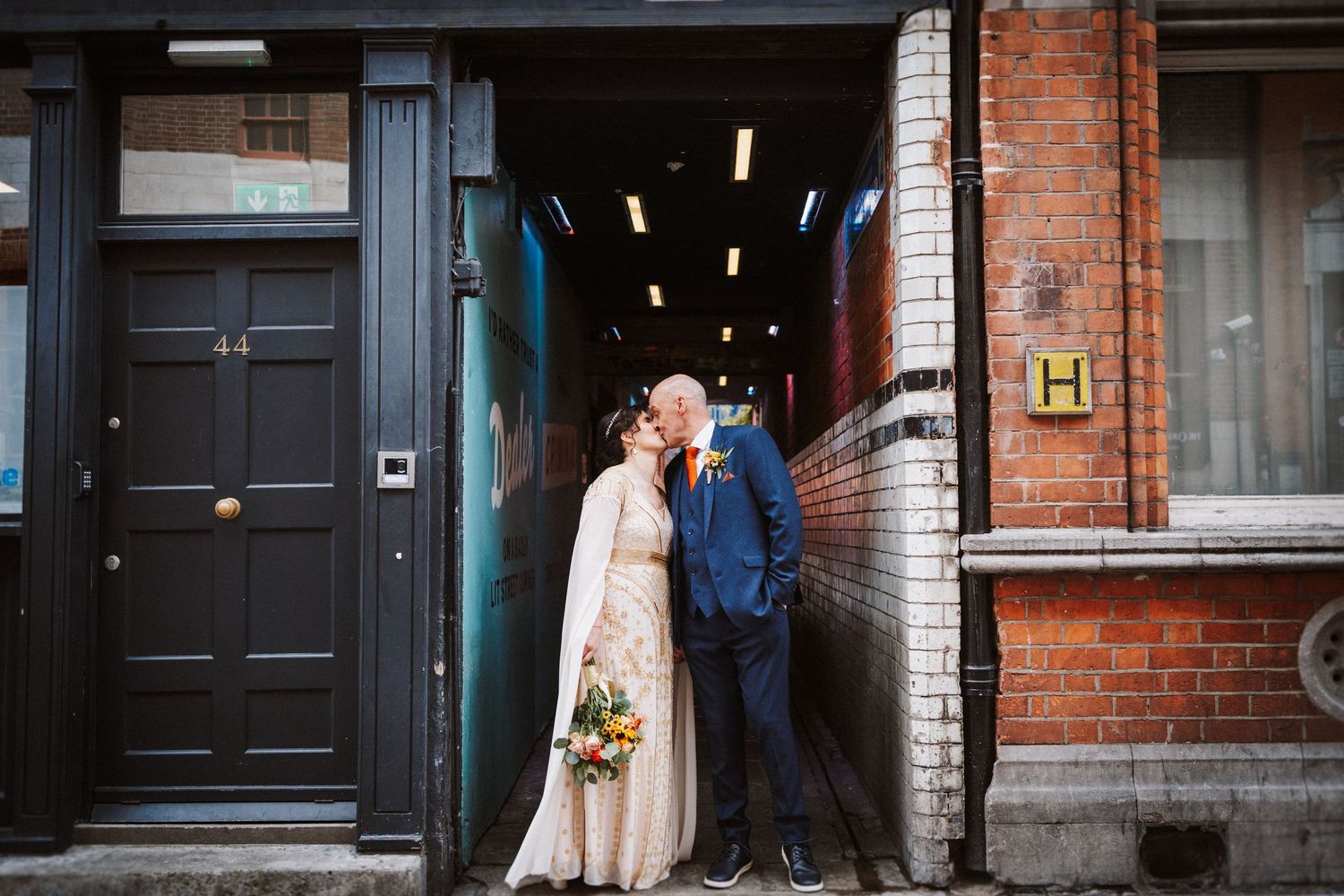 Couple kissing in a romantic winter moment outside a vintage brick building entrance with wreath decor.