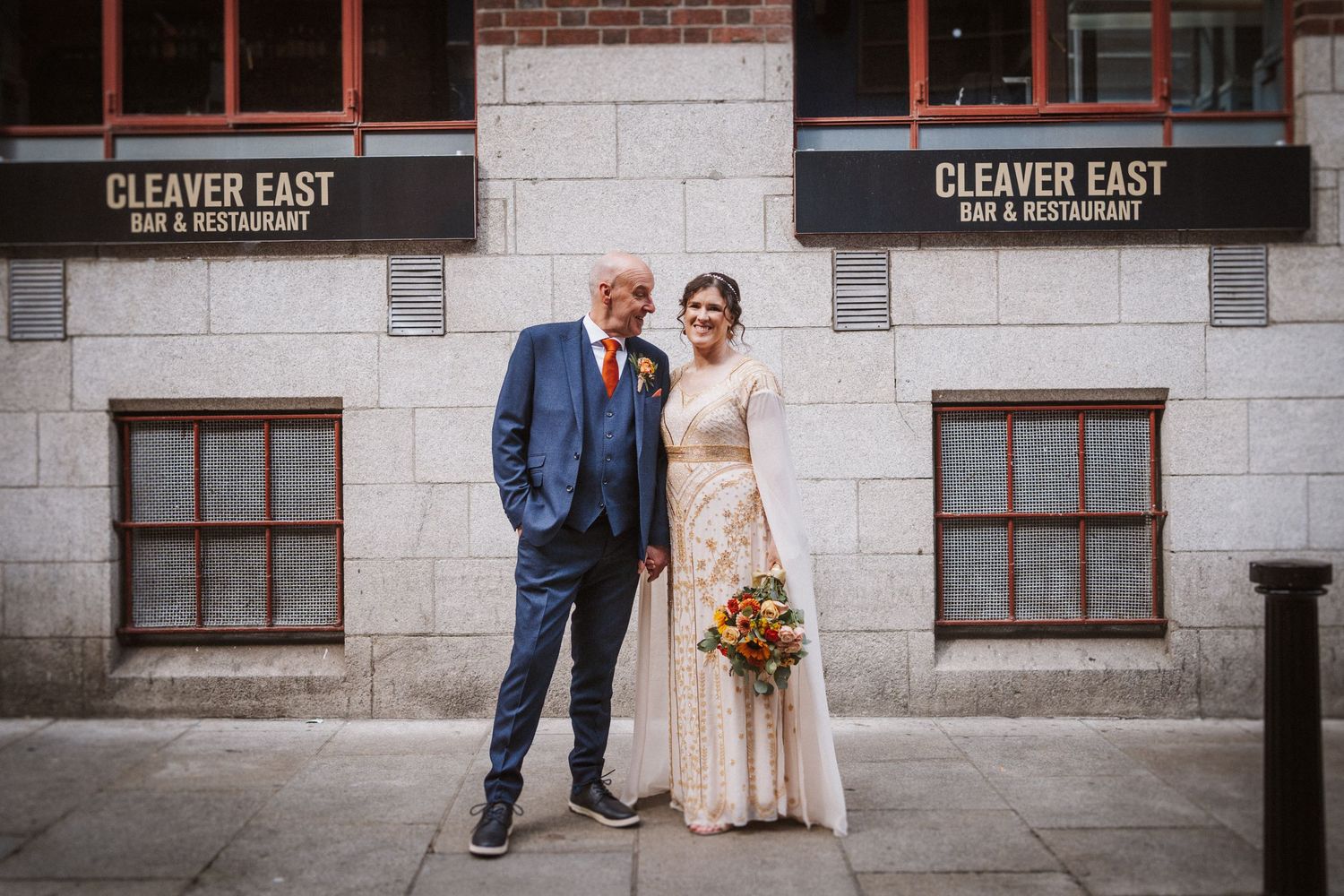 Wedding couple stands together against a brick and stone wall outside Cleaver East Restaurant in Dublin.