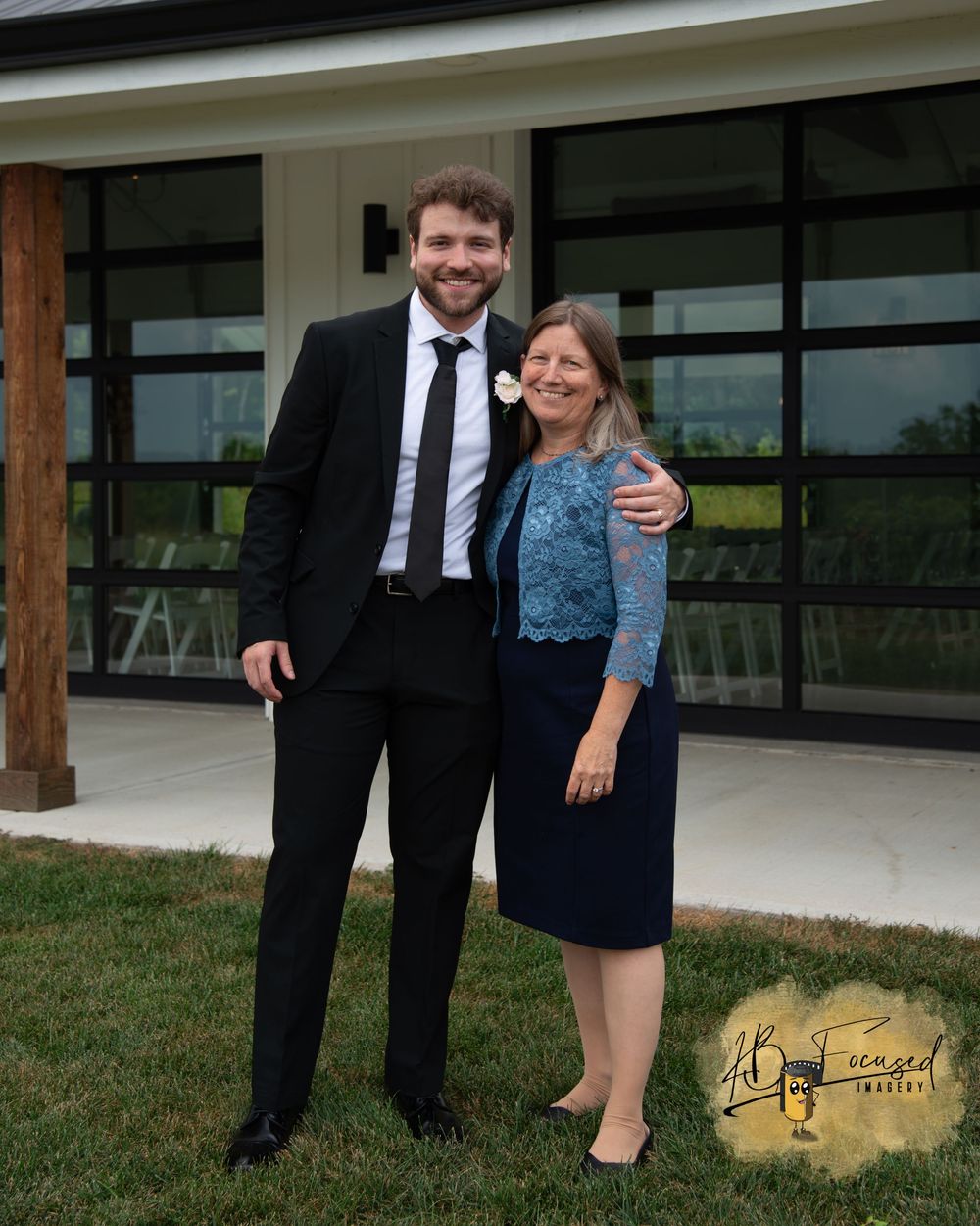 Wedding party members pose together outside a modern building with wooden pillars.