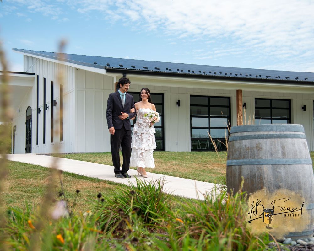 Rustic outdoor wedding venue with wine barrels and white buildings.