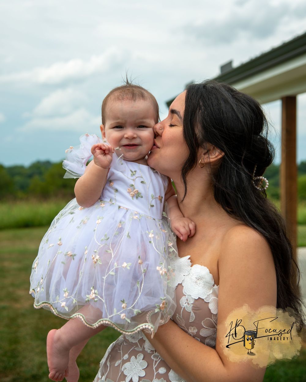 A sweet moment outdoors with a baby in a white lace dress against a cloudy sky.