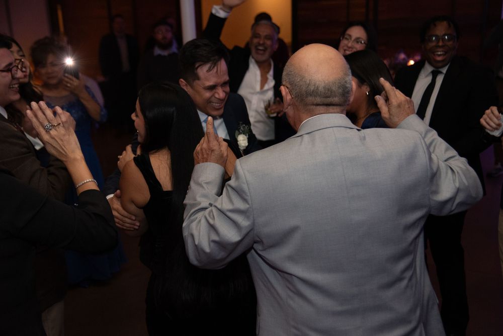 Wedding reception guests dancing and celebrating in a dimly lit venue.