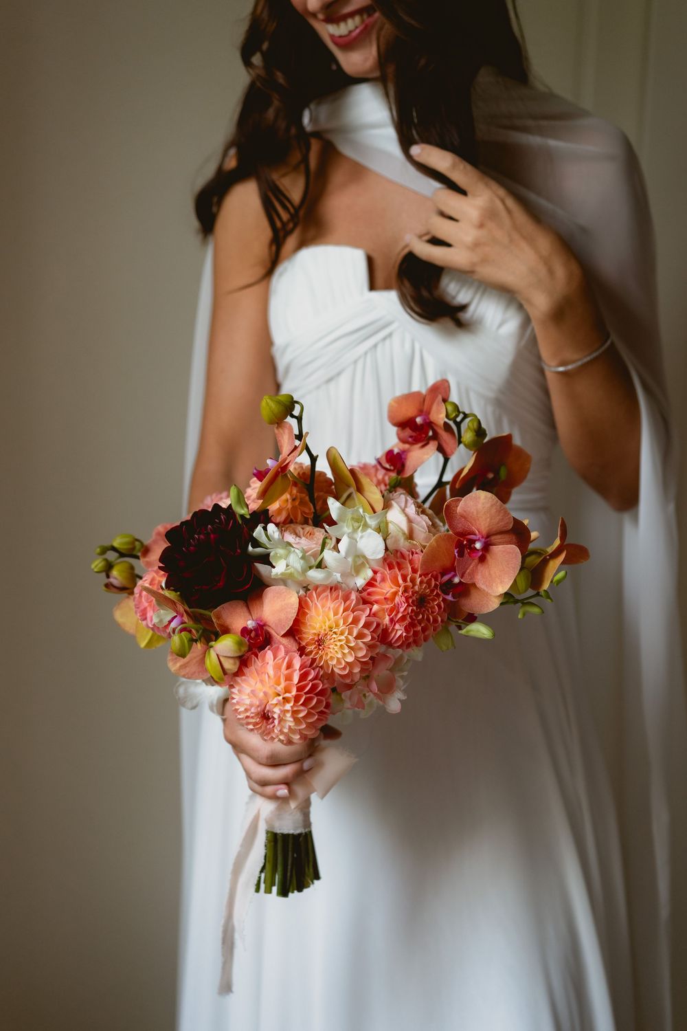 A beautiful coral and pink wedding bouquet held against a white dress.