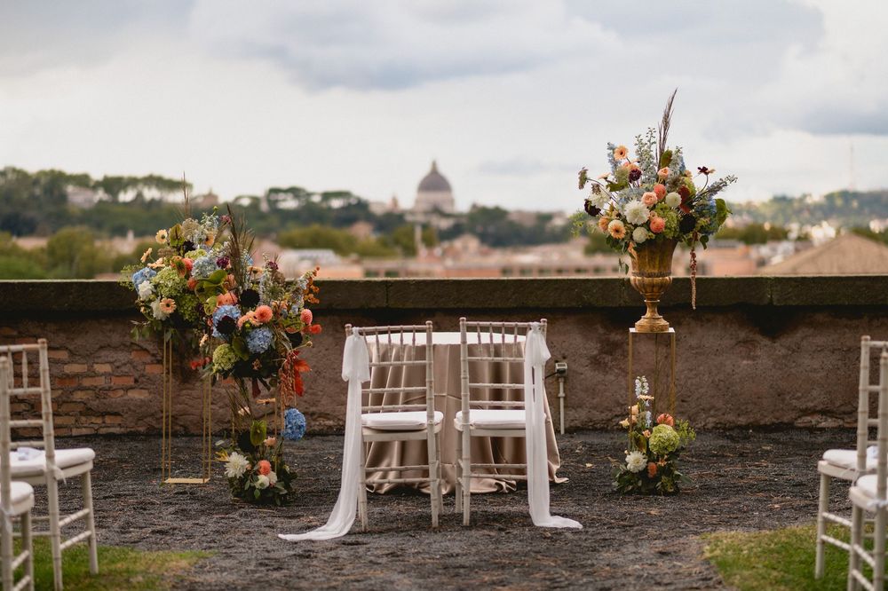 White chairs and floral arrangements set up for an outdoor wedding ceremony with a scenic city backdrop.
