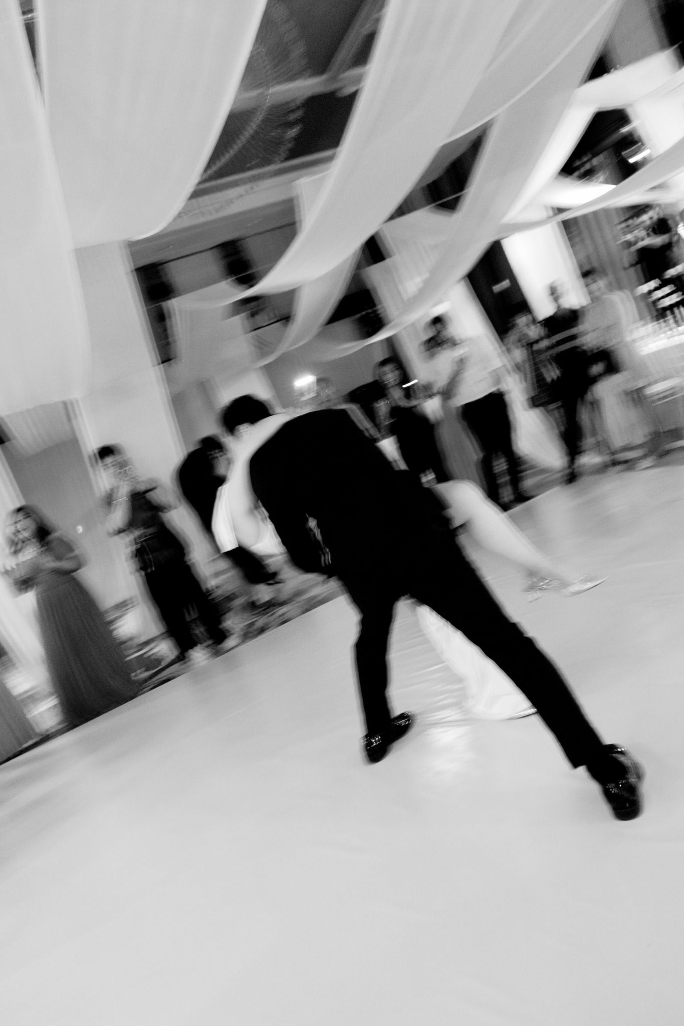 Blurred black and white photo of wedding guests dancing at an elegant reception venue.