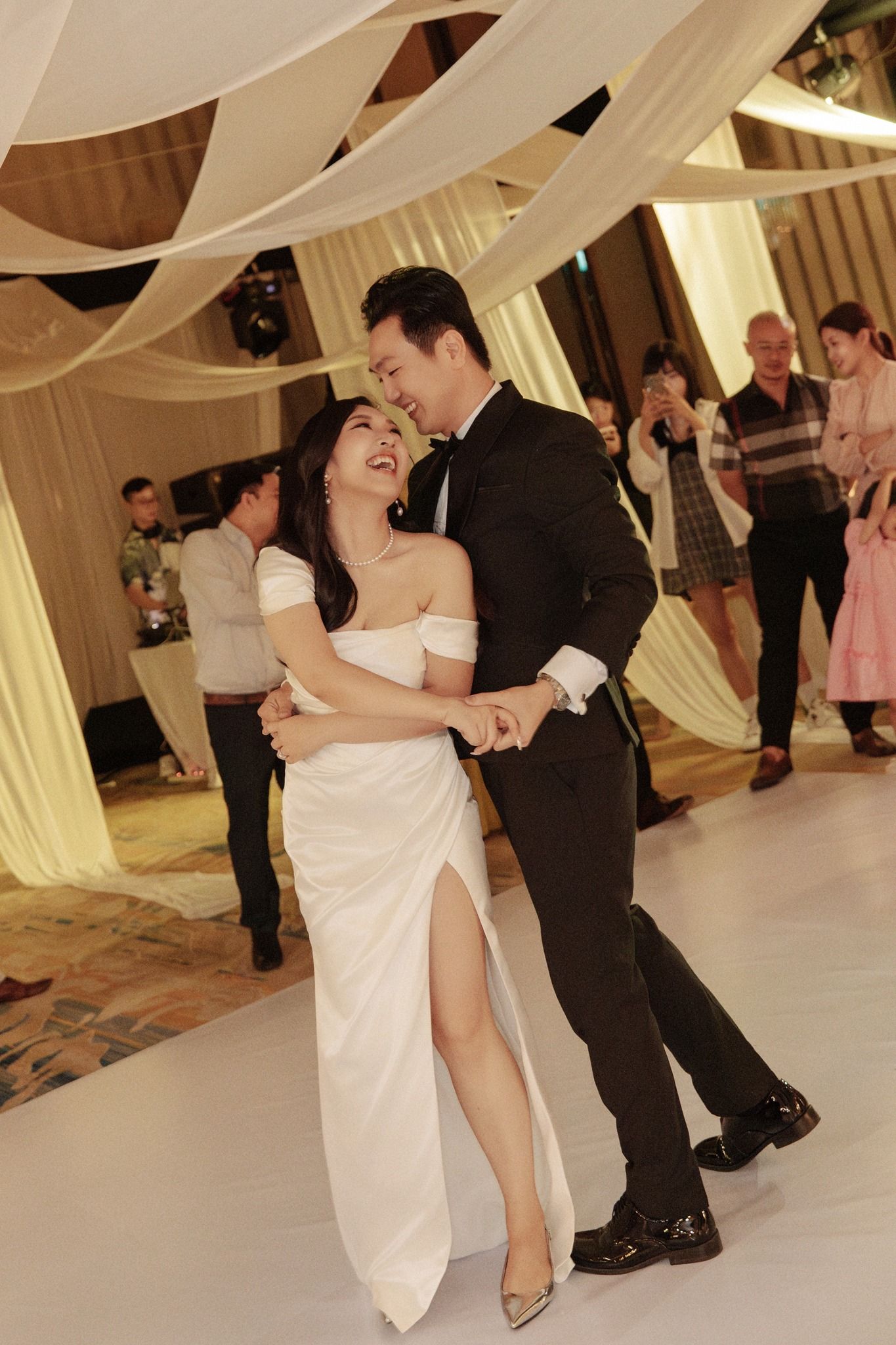 Bride and groom laugh joyfully during their first dance at elegant wedding reception.