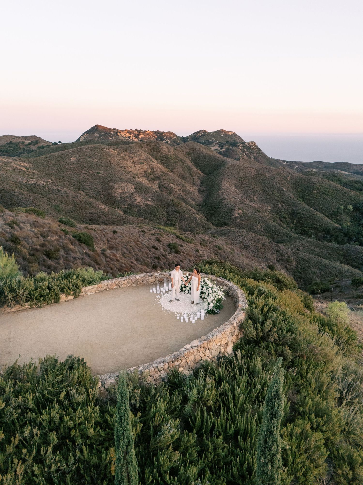 Scenic mountain path curves through rugged California coastal terrain at sunset with cyclists on winding dirt road.
