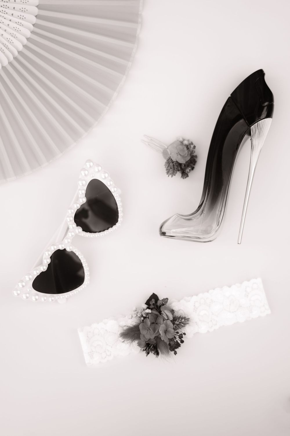 Black and white still life with perfume bottle, heart shapes, lace details and paper fan against white background.