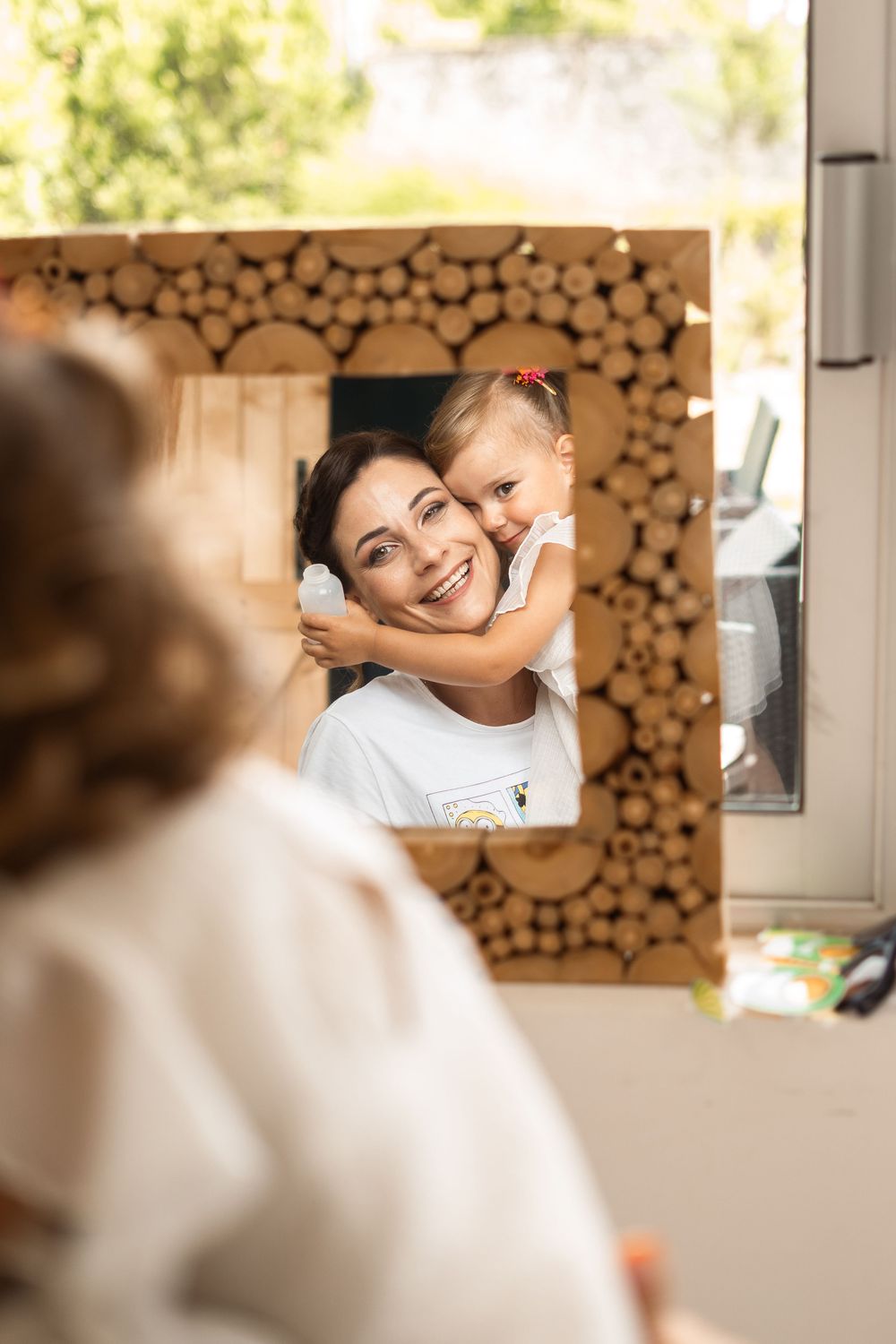 A rustic wooden frame with circular log details reflects a tender moment in a mirror.