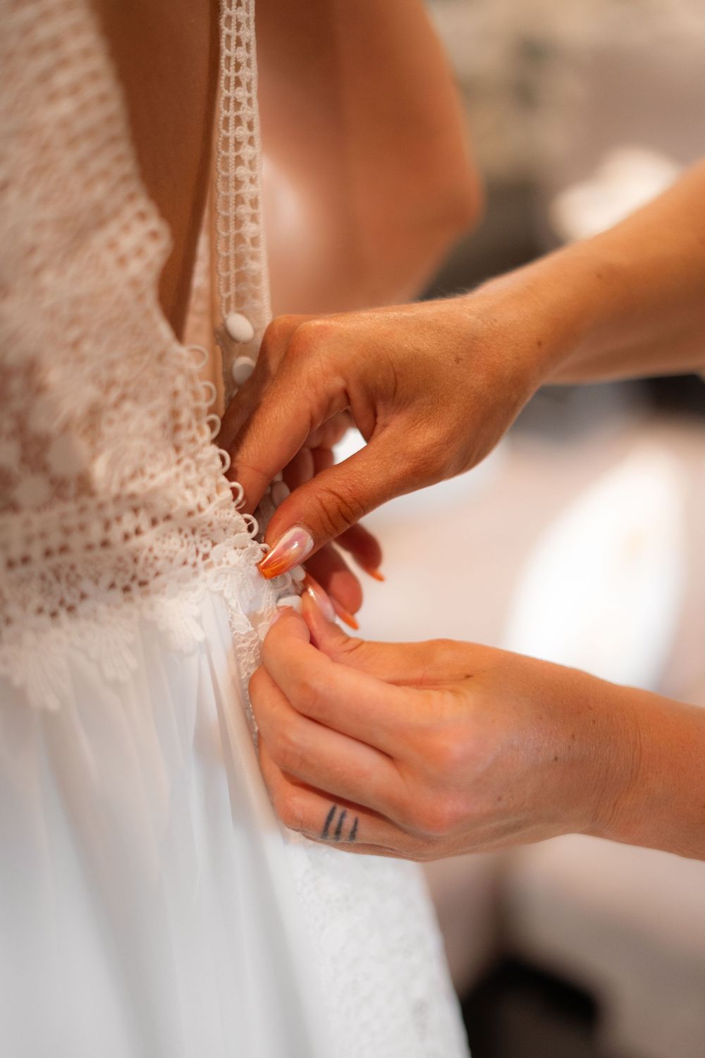 Hands fastening delicate buttons and lace details on an elegant white wedding dress.