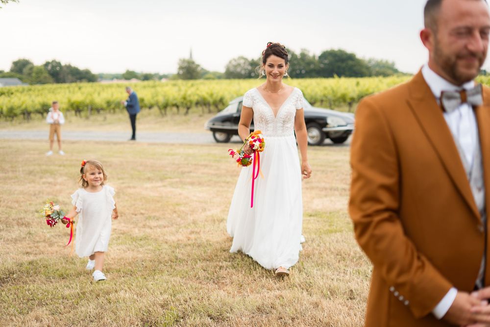 Wedding party walking through a sunny vineyard field on a bright summer day.