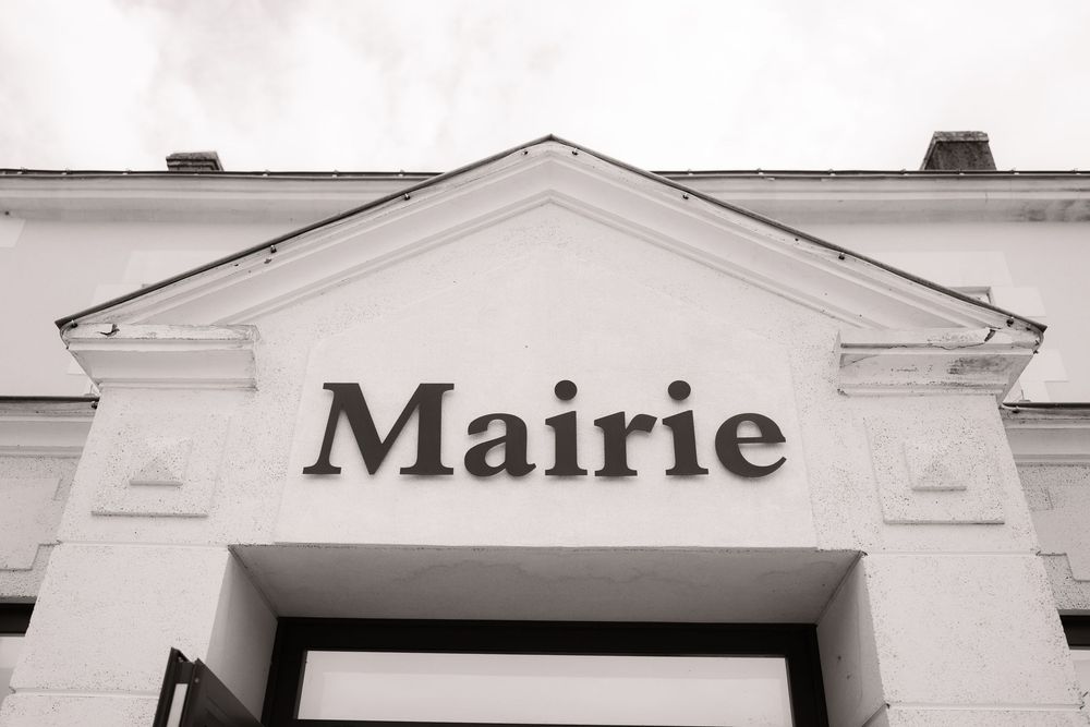 A series of white building facades with classic French architecture showing 'Mairie' text on one segment.