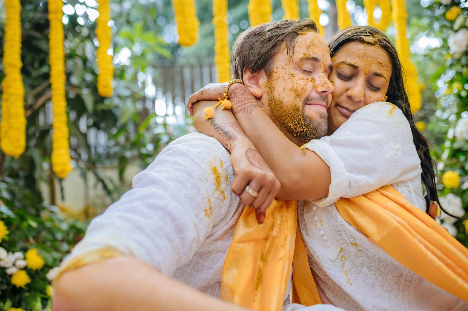 Bride and groom covered in turmeric during an Indo-Norwegian wedding and Family applying Haldi to the bride during a joyful wedding ritual