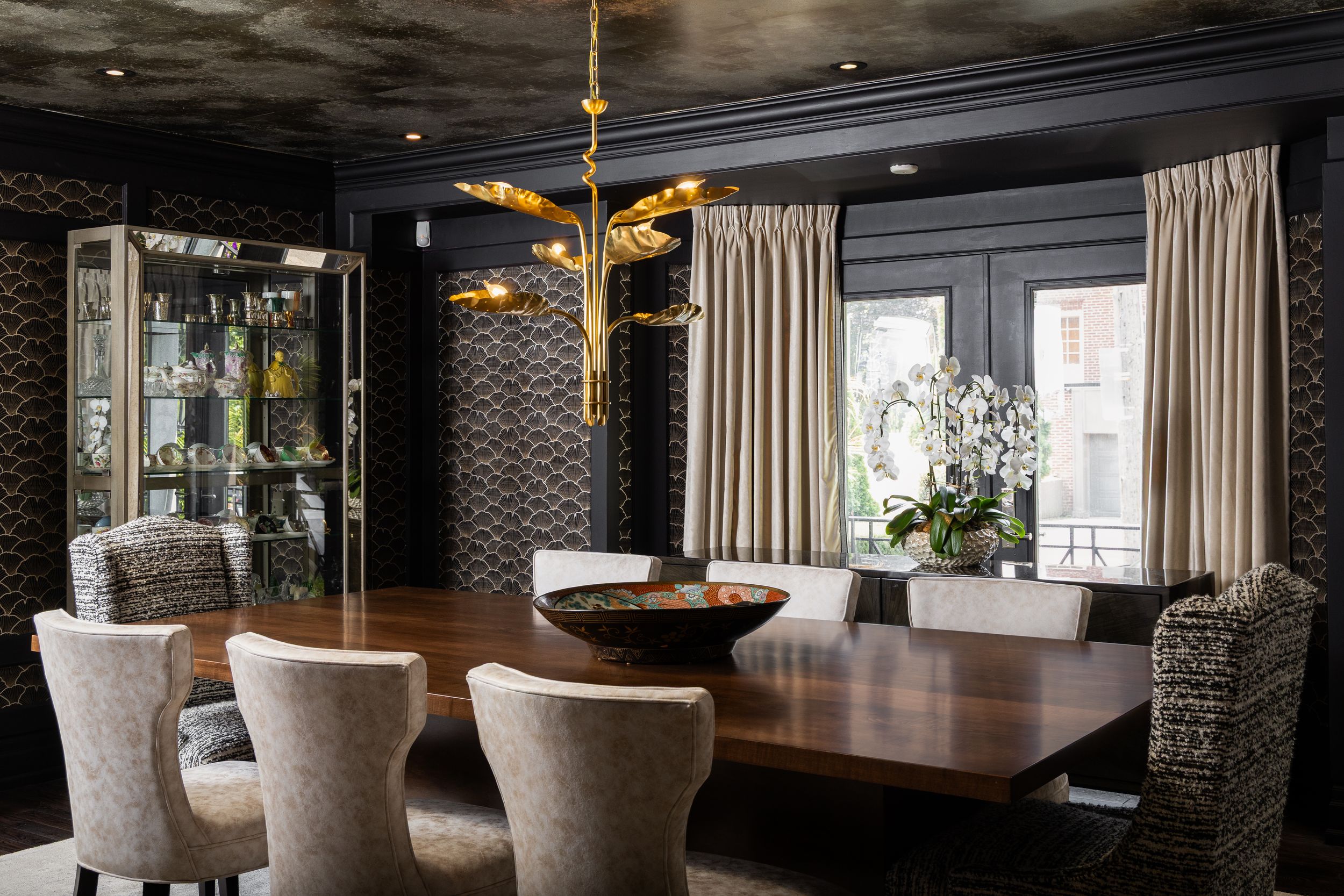 Elegant modern dining room features a long wooden table and upholstered chairs beneath dramatic dark pendant lighting.