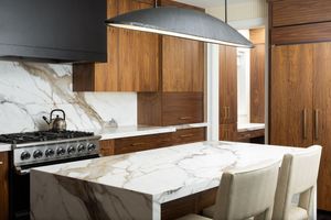 Modern kitchen interior with white marble backsplash, wooden cabinets, and track lighting creates a sleek minimalist design.