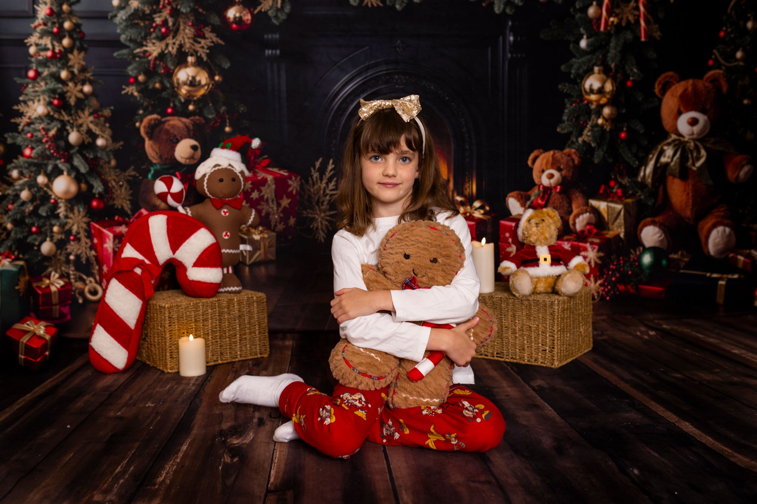 PHOTOGRAPH OF A MUM DAD AND TWO BABAY GIRLS SITTING ON A COUCH IN A COSY ROOM DECORATED FOR CHRISTMAS