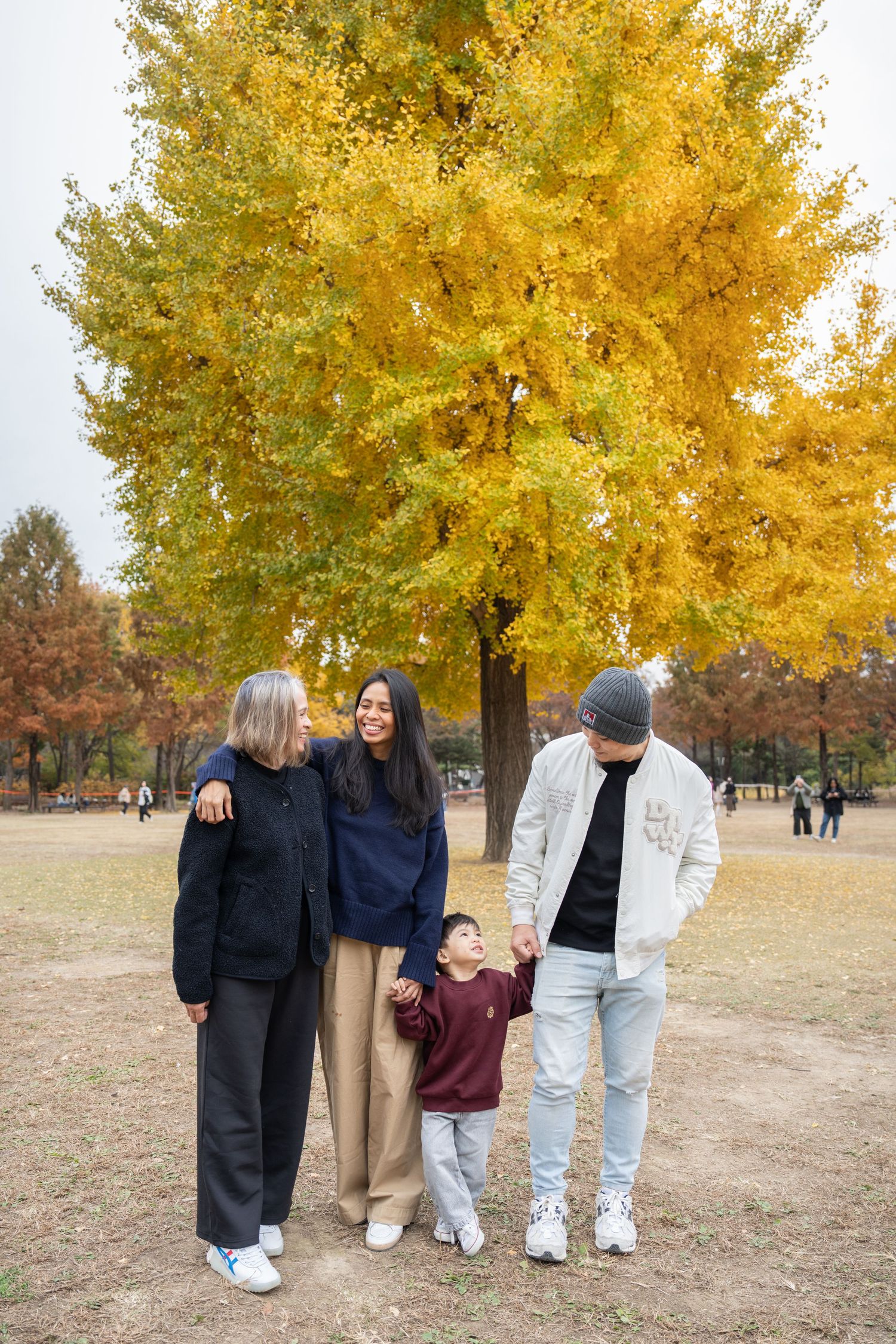 A group of friends walking together in a park with vibrant yellow fall foliage trees in the background.